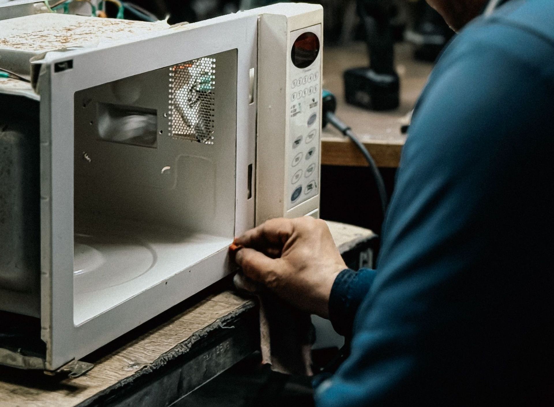 An adult male fixing a microwave in a cluttered workshop, focusing on repairs.